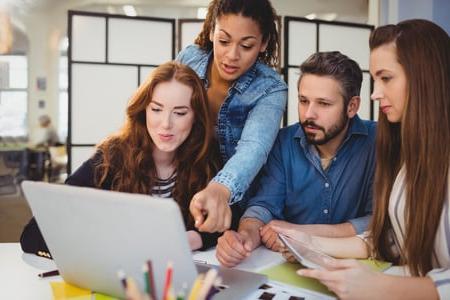 Businesswoman pointing at laptop with coworkers at desk in creative office